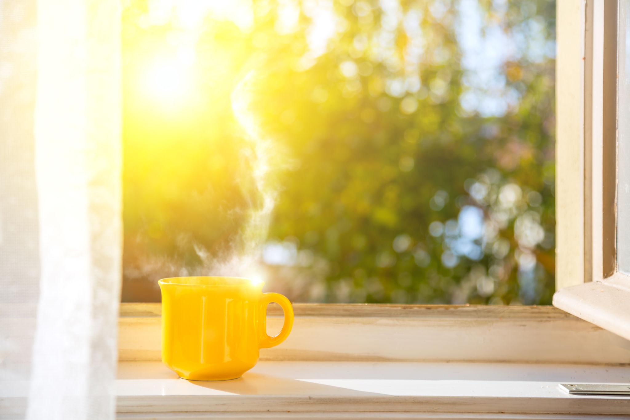 Xícara amarela de café iluminada pelo sol junto a uma janela